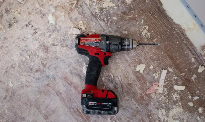 Design reference: a cordless drill on a stripped wall during the rough-in phase of a remodel, before new surfaces go in