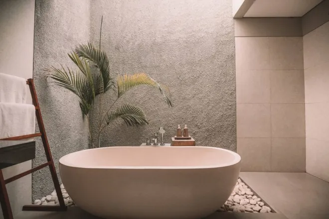 Design reference: stone-colored freestanding oval tub set against a textured plaster wall with a pebble border