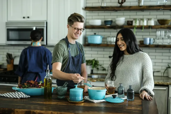 Design reference: people cooking together in a kitchen with white subway tile, open timber shelving and a stainless wall oven