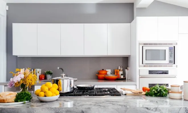 Design reference: handleless white upper cabinets against a grey wall above a marble countertop and a gas cooktop