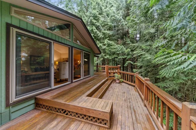 Design reference: a wood deck with a built-in perimeter bench wrapping a house surrounded by evergreen trees, the shaded damp setting a Northwest deck has to survive