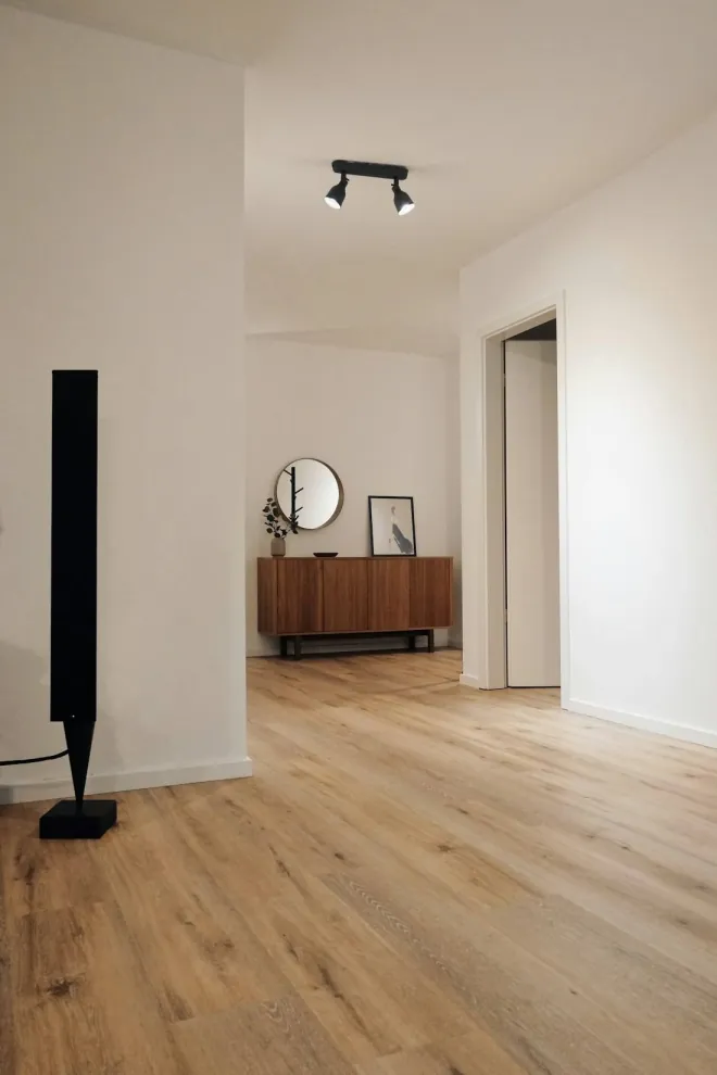 Design reference: empty room with new light wood flooring, a round mirror, and a low wood console against a white wall
