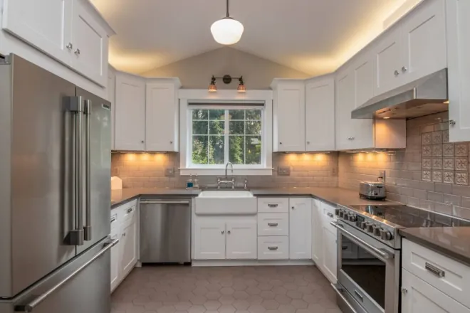 Design reference: a white shaker kitchen with an apron-front sink under a window and a range along the same wall, showing sink and range placement