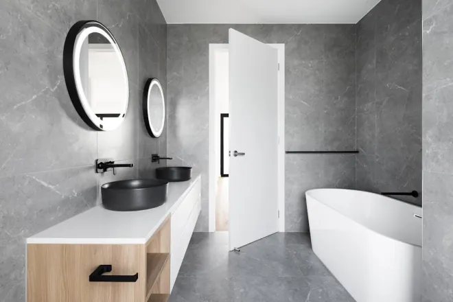 Design reference: grey stone-look bathroom with a floating wood vanity, two round black vessel basins, round mirrors